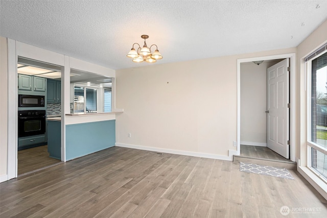 interior space with a notable chandelier, a textured ceiling, baseboards, and wood finished floors