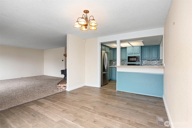 interior space with open floor plan, freestanding refrigerator, blue cabinets, black microwave, and backsplash