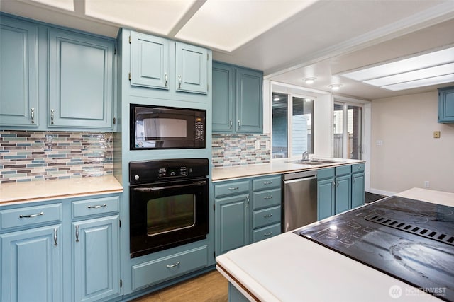 kitchen with blue cabinetry, light countertops, backsplash, a sink, and black appliances