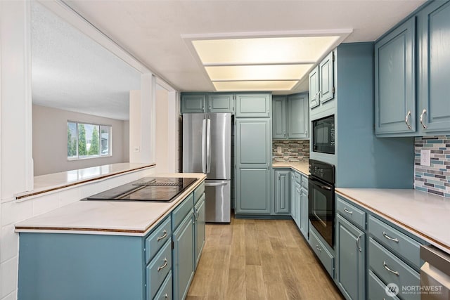 kitchen with black appliances, backsplash, light countertops, and light wood-style flooring