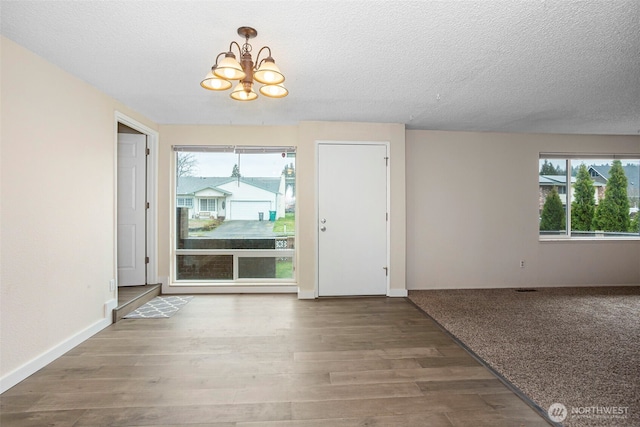 entryway with baseboards, a textured ceiling, an inviting chandelier, and wood finished floors