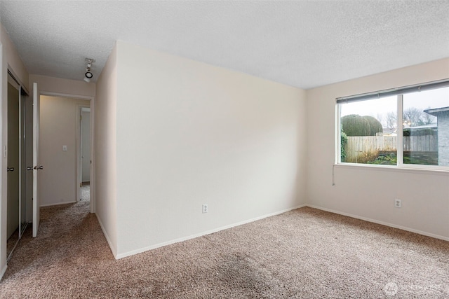 empty room featuring a textured ceiling, carpet floors, and baseboards