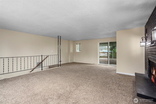 spare room with carpet floors, a brick fireplace, a textured ceiling, and baseboards