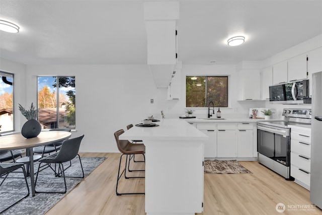 kitchen featuring a breakfast bar area, stainless steel appliances, a peninsula, a sink, and light countertops