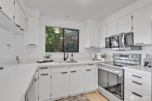 kitchen featuring stainless steel electric range oven, white cabinetry, light countertops, and a sink