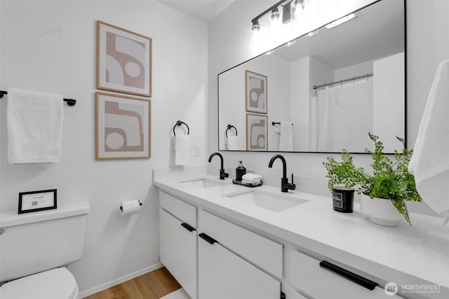 bathroom featuring toilet, double vanity, a sink, and wood finished floors