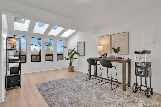 office area with lofted ceiling with skylight, baseboards, and wood finished floors