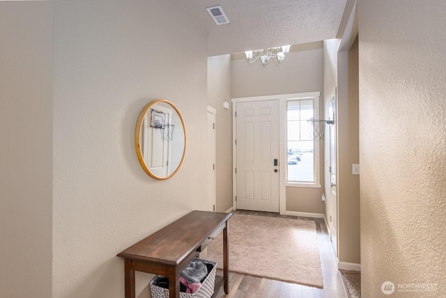 entrance foyer featuring baseboards, visible vents, wood finished floors, a textured ceiling, and a chandelier