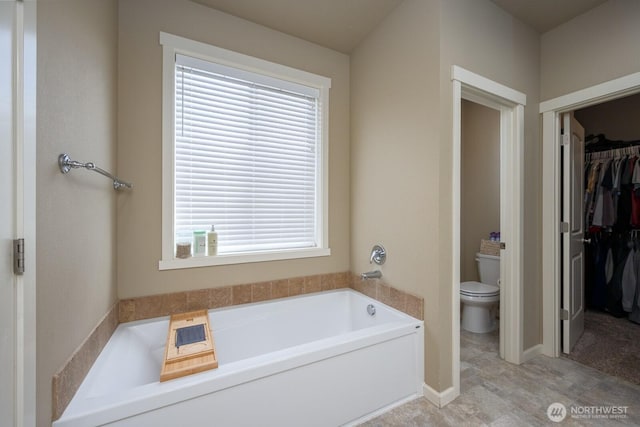 full bathroom with toilet, a garden tub, a spacious closet, and baseboards