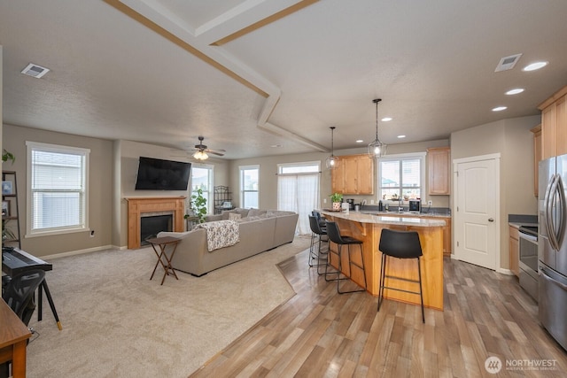 kitchen with visible vents, open floor plan, a kitchen bar, light brown cabinets, and a fireplace