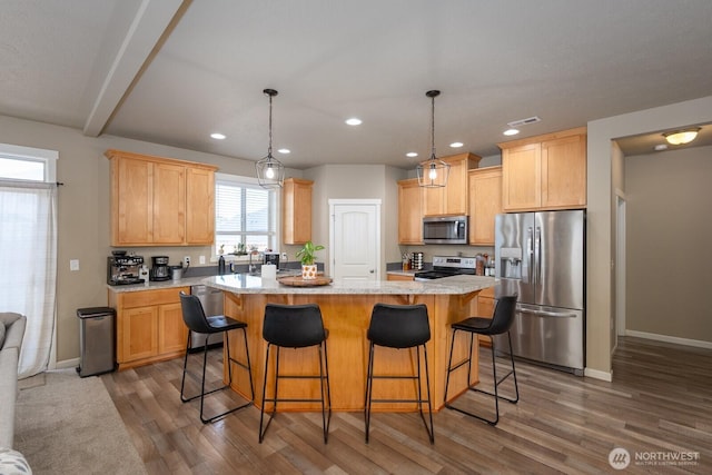 kitchen with wood finished floors, baseboards, appliances with stainless steel finishes, a center island, and light brown cabinetry