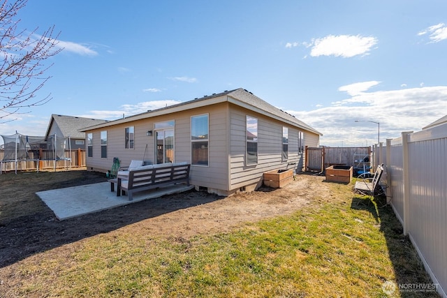 rear view of house featuring a trampoline, a yard, a patio, crawl space, and a fenced backyard