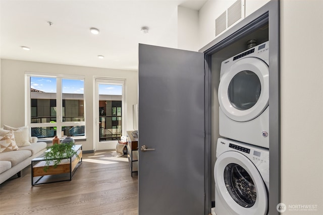 clothes washing area featuring stacked washing maching and dryer, visible vents, laundry area, and wood finished floors