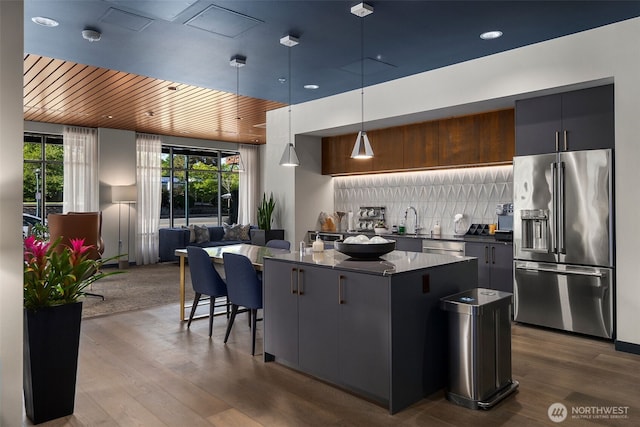 kitchen featuring high end refrigerator, decorative backsplash, dark countertops, a kitchen island, and dark wood-type flooring