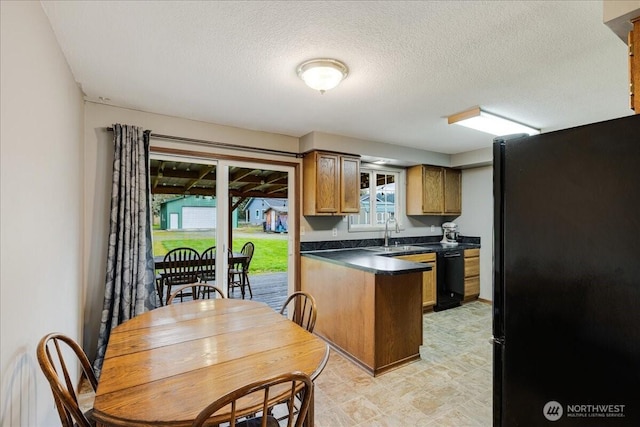 kitchen featuring black appliances, a sink, dark countertops, a peninsula, and brown cabinetry