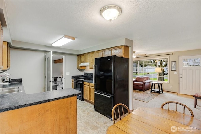 kitchen with black appliances, a sink, under cabinet range hood, dark countertops, and a peninsula