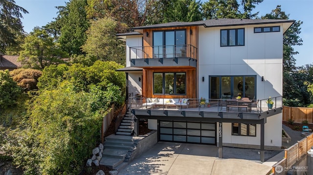 back of property with stairway, a balcony, fence, concrete driveway, and a garage