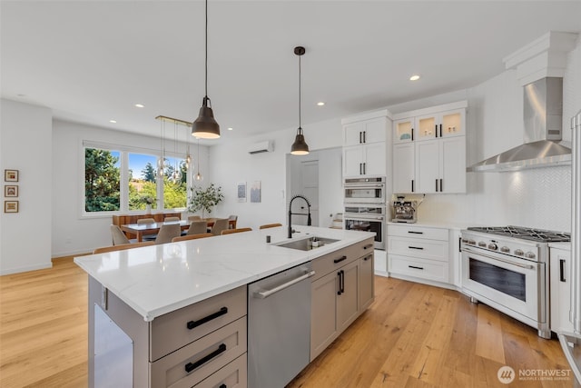 kitchen with a kitchen island with sink, a sink, stainless steel appliances, wall chimney exhaust hood, and tasteful backsplash