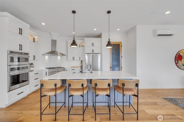 kitchen featuring a wall mounted air conditioner, a sink, a kitchen breakfast bar, stainless steel appliances, and wall chimney range hood