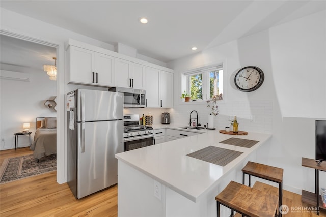 kitchen featuring a peninsula, a sink, appliances with stainless steel finishes, a kitchen bar, and backsplash