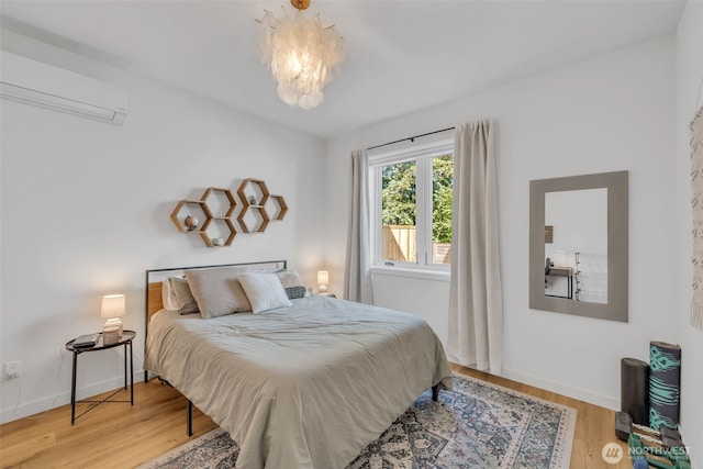 bedroom with a notable chandelier, baseboards, a wall unit AC, and wood finished floors