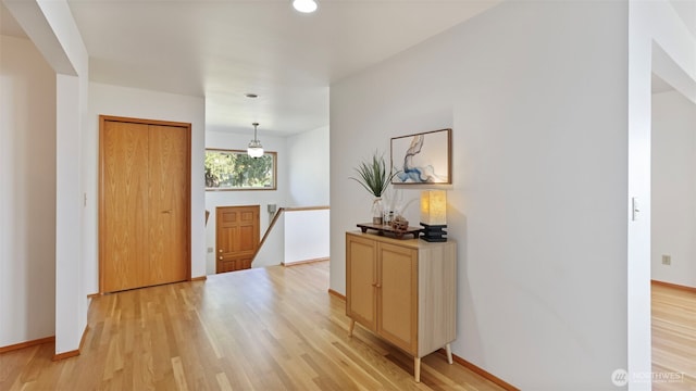 hall featuring baseboards, light wood finished floors, and an upstairs landing