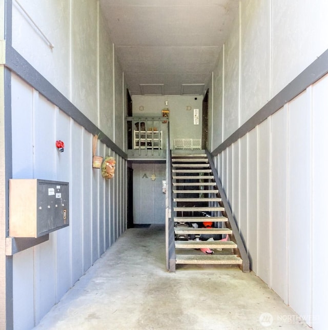 stairway featuring mail area and unfinished concrete floors