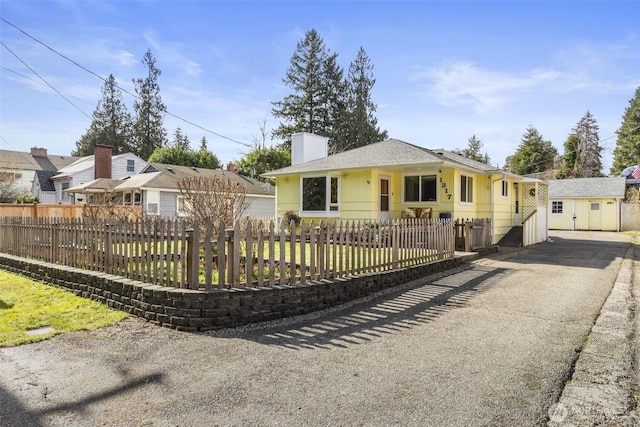 view of front of property featuring a fenced front yard, a chimney, and an outdoor structure