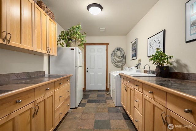 kitchen with dark countertops, freestanding refrigerator, stone finish floor, washing machine and dryer, and a sink