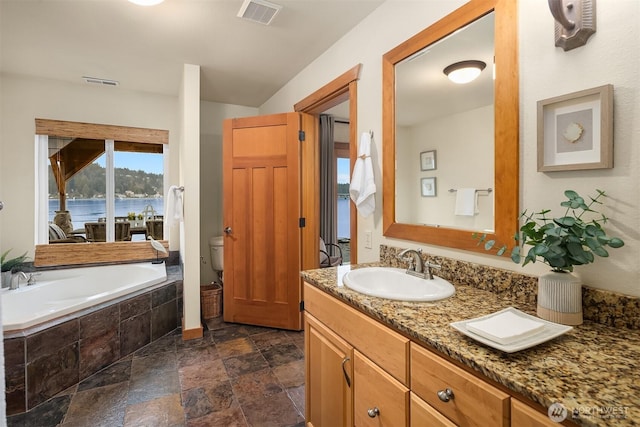 bathroom with stone tile floors, visible vents, toilet, vanity, and a bath