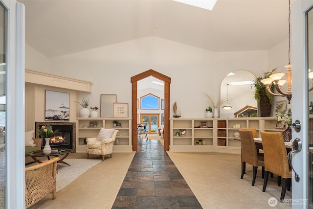 living area with a lit fireplace, vaulted ceiling, and stone tile floors