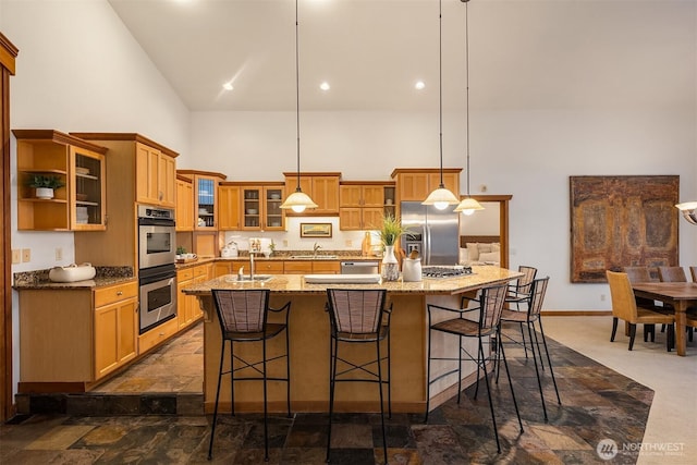 kitchen with stainless steel appliances, a sink, a towering ceiling, a kitchen bar, and a large island with sink