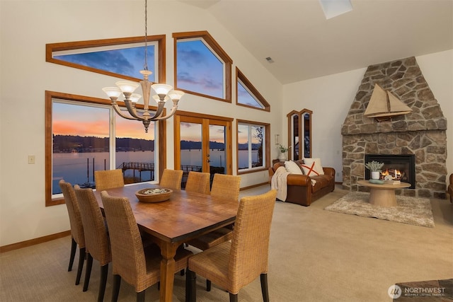 carpeted dining space with visible vents, a chandelier, a stone fireplace, french doors, and high vaulted ceiling