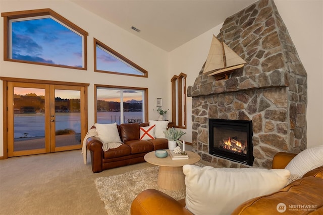 living room with carpet, french doors, a water view, visible vents, and a stone fireplace