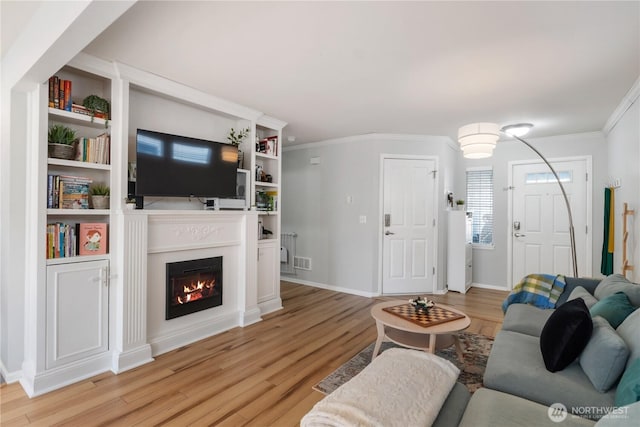 living area featuring baseboards, a lit fireplace, light wood-type flooring, and crown molding