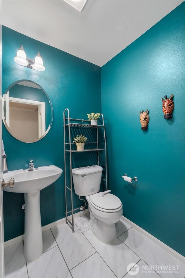 half bath featuring marble finish floor, toilet, and baseboards