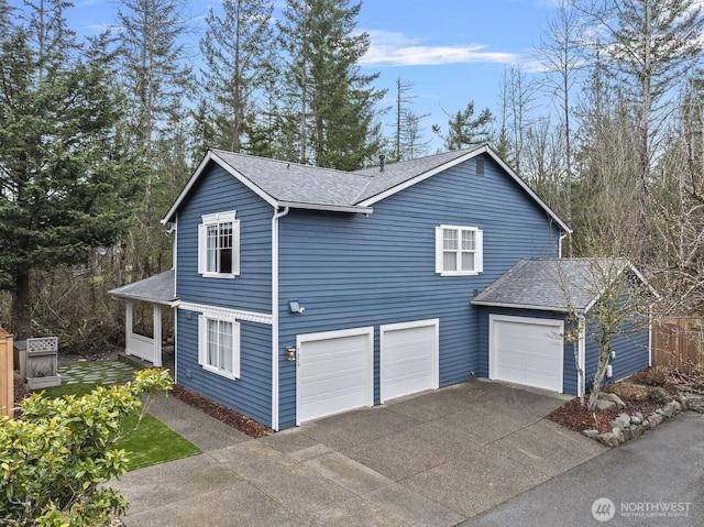 view of side of property featuring a garage, roof with shingles, and driveway