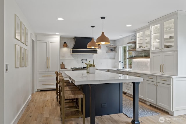 kitchen featuring light wood finished floors, decorative backsplash, white cabinetry, and custom range hood