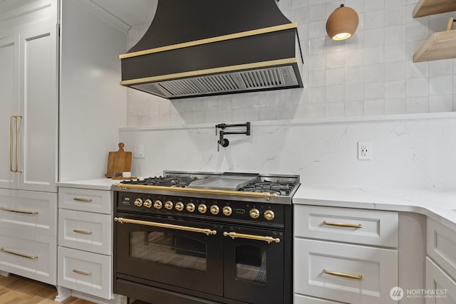 kitchen featuring range with two ovens, custom exhaust hood, white cabinetry, and decorative backsplash