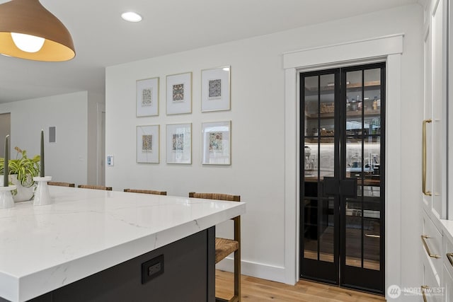 kitchen featuring light wood finished floors, baseboards, white cabinets, light stone counters, and a breakfast bar area