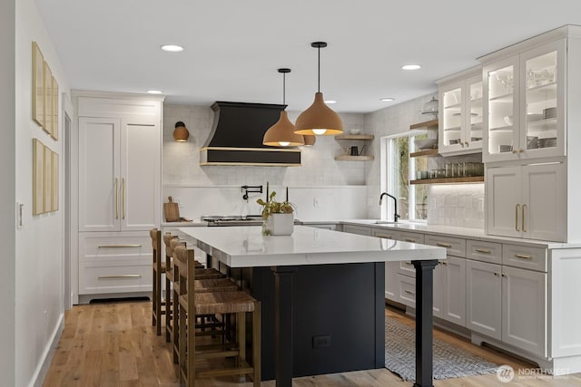 kitchen with a breakfast bar, light wood-style floors, premium range hood, white cabinetry, and open shelves