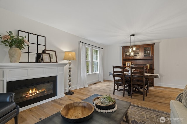 dining space featuring light wood-type flooring, a glass covered fireplace, visible vents, and baseboards