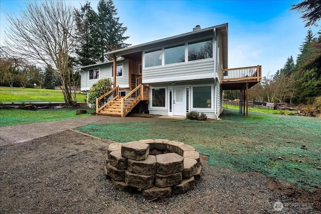 back of property with a deck, a fire pit, stairs, a lawn, and a chimney