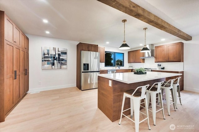 kitchen with light wood-style flooring, stainless steel appliances, a kitchen breakfast bar, wall chimney range hood, and beamed ceiling