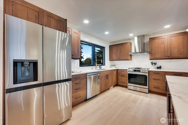 kitchen featuring stainless steel appliances, wall chimney range hood, light wood-style floors, and tasteful backsplash