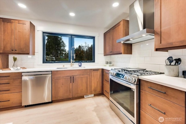 kitchen with stainless steel appliances, wall chimney range hood, a sink, and brown cabinets