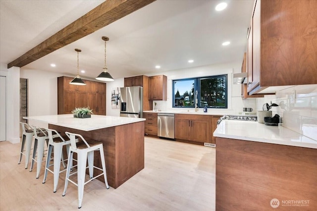 kitchen with brown cabinets, beamed ceiling, a center island, a kitchen breakfast bar, and stainless steel appliances