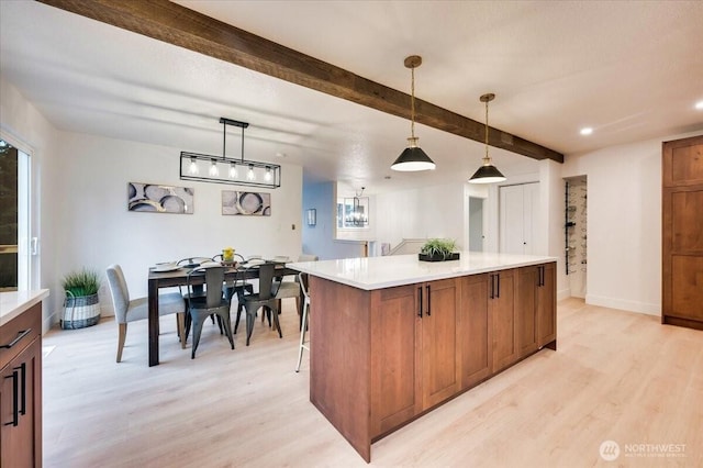 kitchen featuring a center island, brown cabinets, light countertops, light wood-style flooring, and beamed ceiling