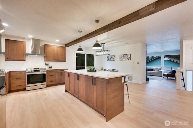 kitchen featuring stainless steel range with gas cooktop, decorative backsplash, light wood-style floors, wall chimney range hood, and beamed ceiling