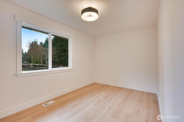 empty room with baseboards, visible vents, and light wood finished floors